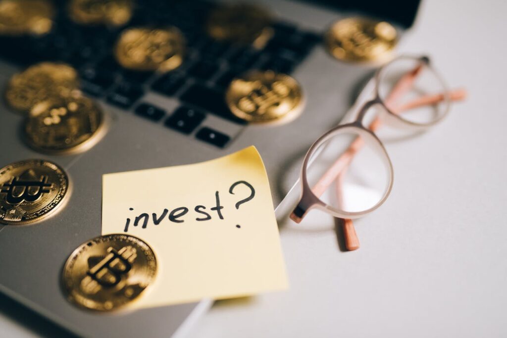 pexels photo 8919575 A close-up of bitcoin coins on a laptop with eyeglasses and a sticky note reading 'invest?'